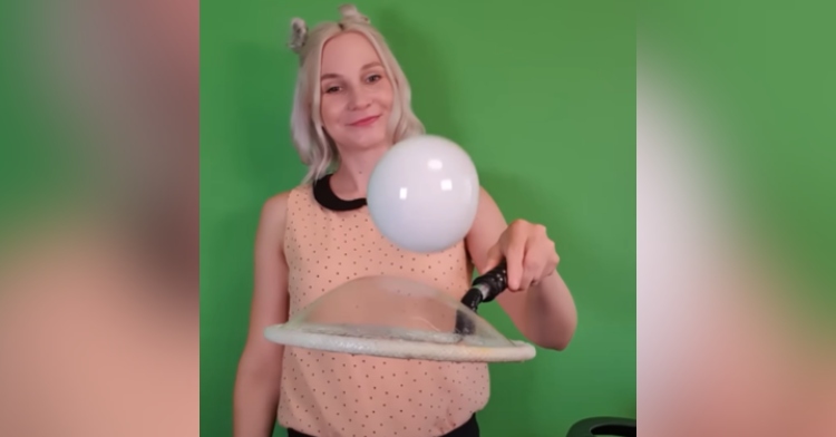 Woman smiles as she bounces a soap bubble on a tennis racket made from yet another bubble.