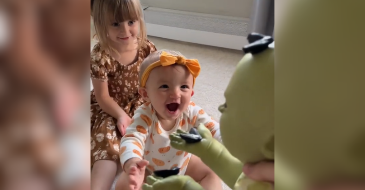 two little girls smile at green toy