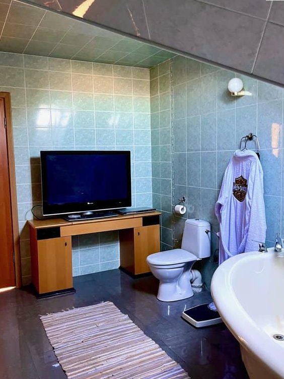 A bathroom with an entertainment center with a TV on top that's right next to the toilet.