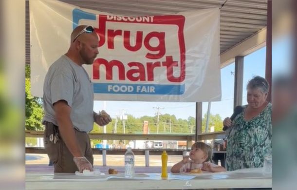 Hot Dog eating contest between a tiny tot and a huge opponent.