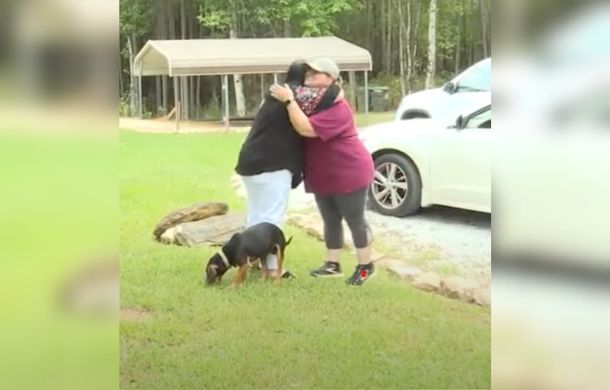 Image shows two women embracing with a black and tan beagle near their feet. The meeting was prompted after mail carrier Holle Prigmore saved the dog's life. The second woman is Kelsey Proctor, the owner of the dog, Ginger.