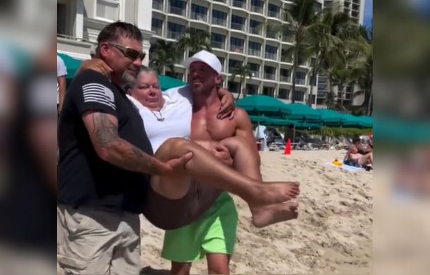 two men carrying a wheelchair-bound woman to swim in the ocean for the first time.