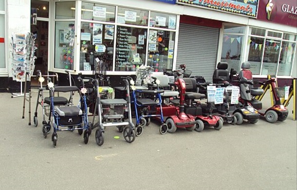 Stock image shows a display of different types of mobility devices including wheelchairs, walkers, and electric scooters.