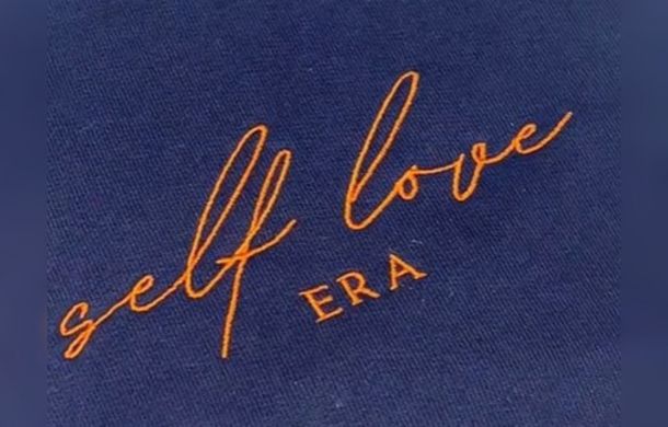 Image shows a shirt design that says "Self Love ERA." The design is being used on a clothing line to replace the use of paper scrubs in psychiatric facilities.