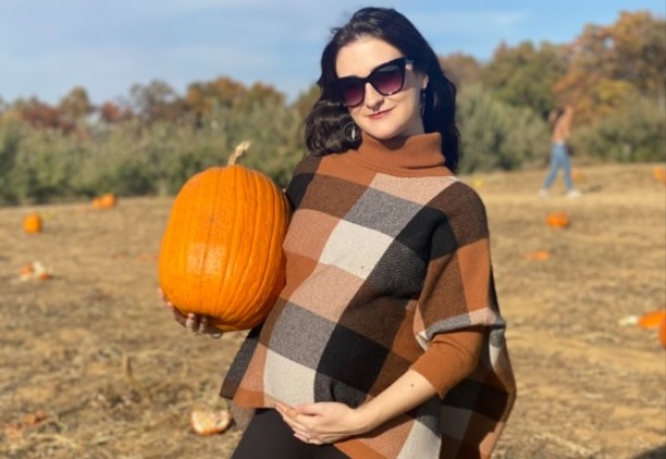 Image shows a pregnant woman wearing a plaid shawl and holding a nicely-shaped oval pumpkin.