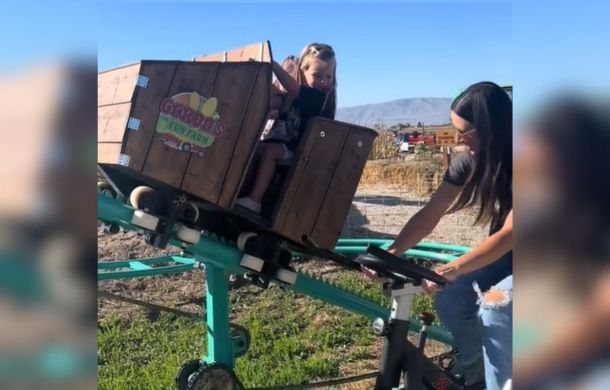 Image shows a parent-powered roller coaster car with two young girls and the mom sitting on a stationary pedaling mechanism.