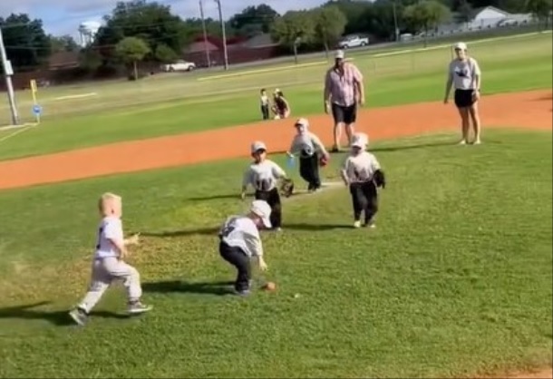 After a hit in a tee ball game, every player tries to grab the ball.