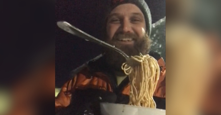 Man smiles as he holds up a bowl of spaghetti. The spaghetti is frozen in the air with the fork stuck there, too