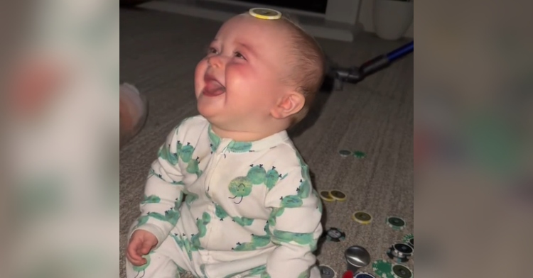 Baby looks up and giggles as she sits on the floor with a poker chip on her head.