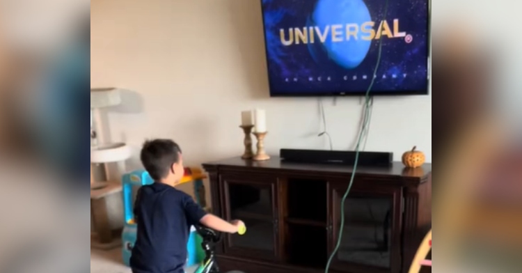 View from behind of a little boy riding a bike in front of a TV.