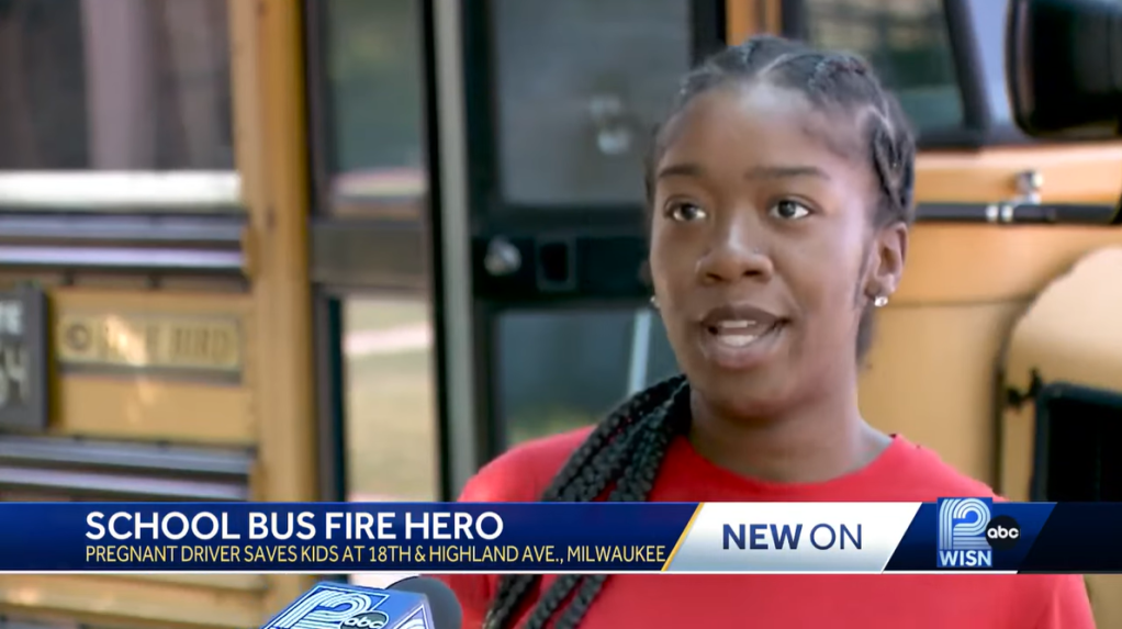 Imunek Williams talking to a new station while standing outside of a school bus.