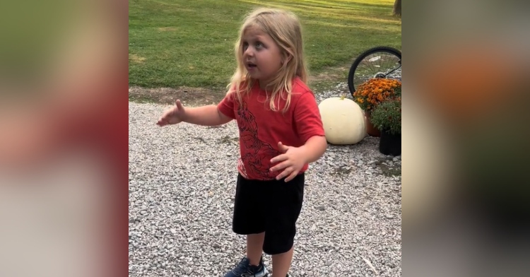 A little boy looks serious as he talks with his hands. He's standing outside.