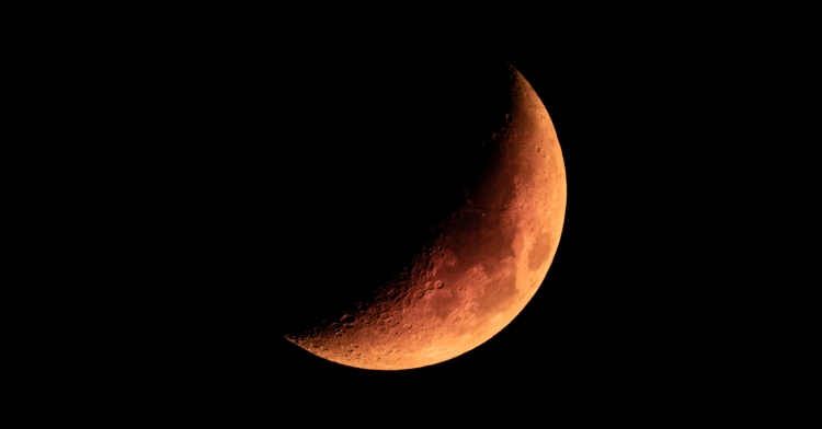 Close up view of the Moon. It has an orange hue and is partially dark because of a partial lunar eclipse.