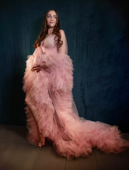Lexi Pratt smiles and looks into the distance while placing her hands on her pregnant stomach. She's wearing a fluffy, semi-sheer pink gown. The background is a dark green that appears to be a sheet. It somehow looks like a legit photoshoot location rather than a hospital.