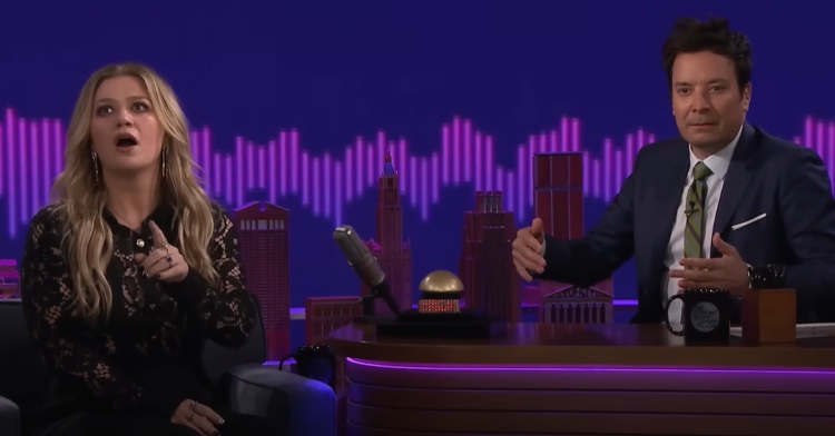 Kelly Clarkson and Jimmy Fallon play a game on the "Tonight Show." Clarkson's mouth is agape and her eyes are wide. Fallon looks unsure as he looks to something off screen.
