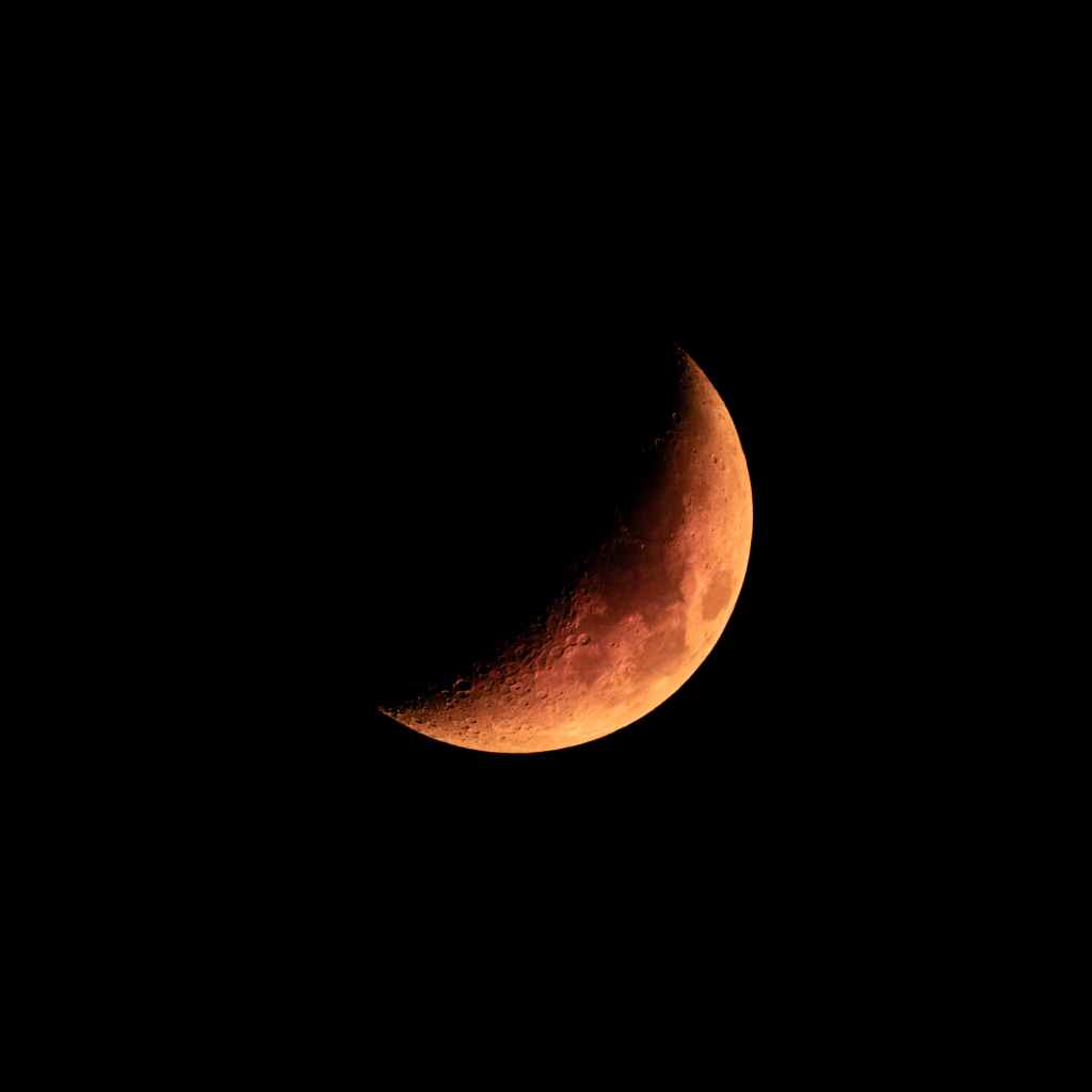 Close up view of the Moon. It has an orange hue and is partially dark because of a partial lunar eclipse.