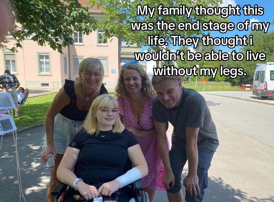 Romy smiles softly from her wheelchair. She is posing for a photo outside with three family members who are smiling. Text on the image reads: "My family thought this was the end stage of my life. They thought I wouldn't be able to live without my legs."