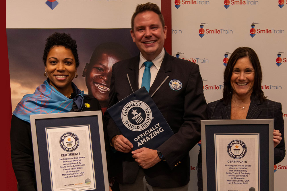 Two women smile and pose next to a man from Guinness World Records, with the two women holding Smile Train's certificates for setting the record for "World's Largest Online Album of Smiling Mouths."