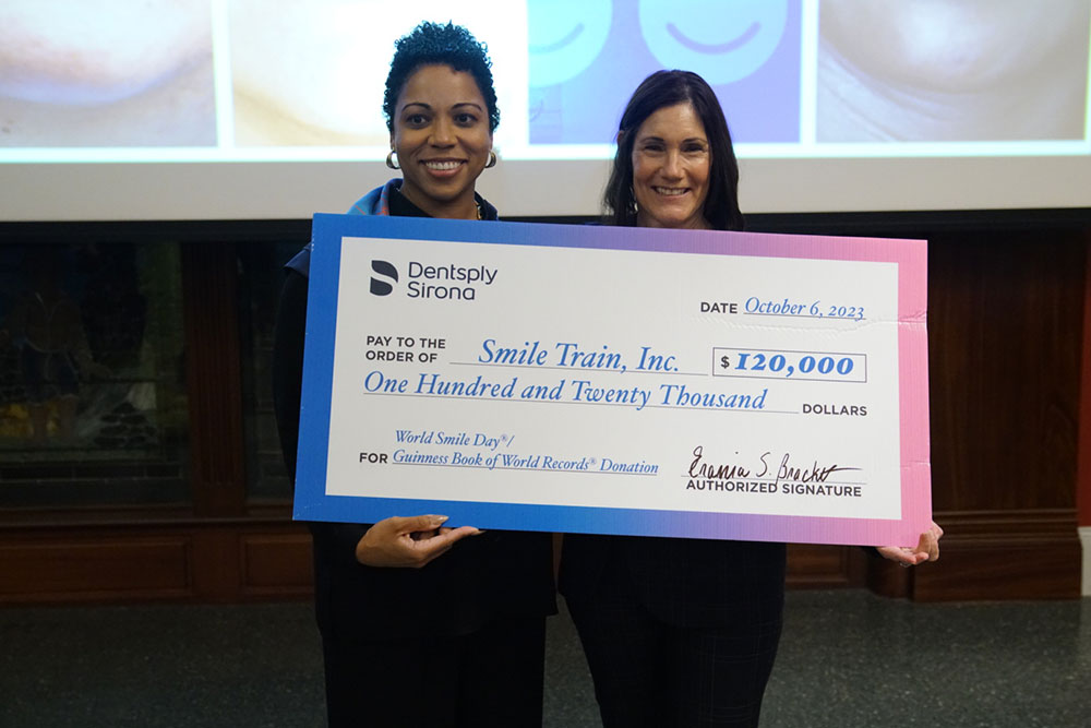 Two women smile as they hold up a giant check from Dentsply Sirona for $120,000 to Smile Train.