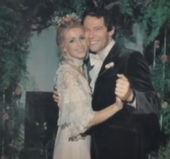 An older photo of Suzanne Somers and Alan Hamel smiling as they hold hands. She's wearing a dress and he's wearing a suit.