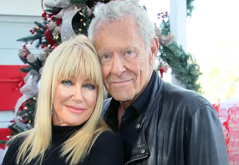 Close up of a more recent photo of Suzanne Somers and Alan Hamel as they smile softly. They're lightly resting their heads together.