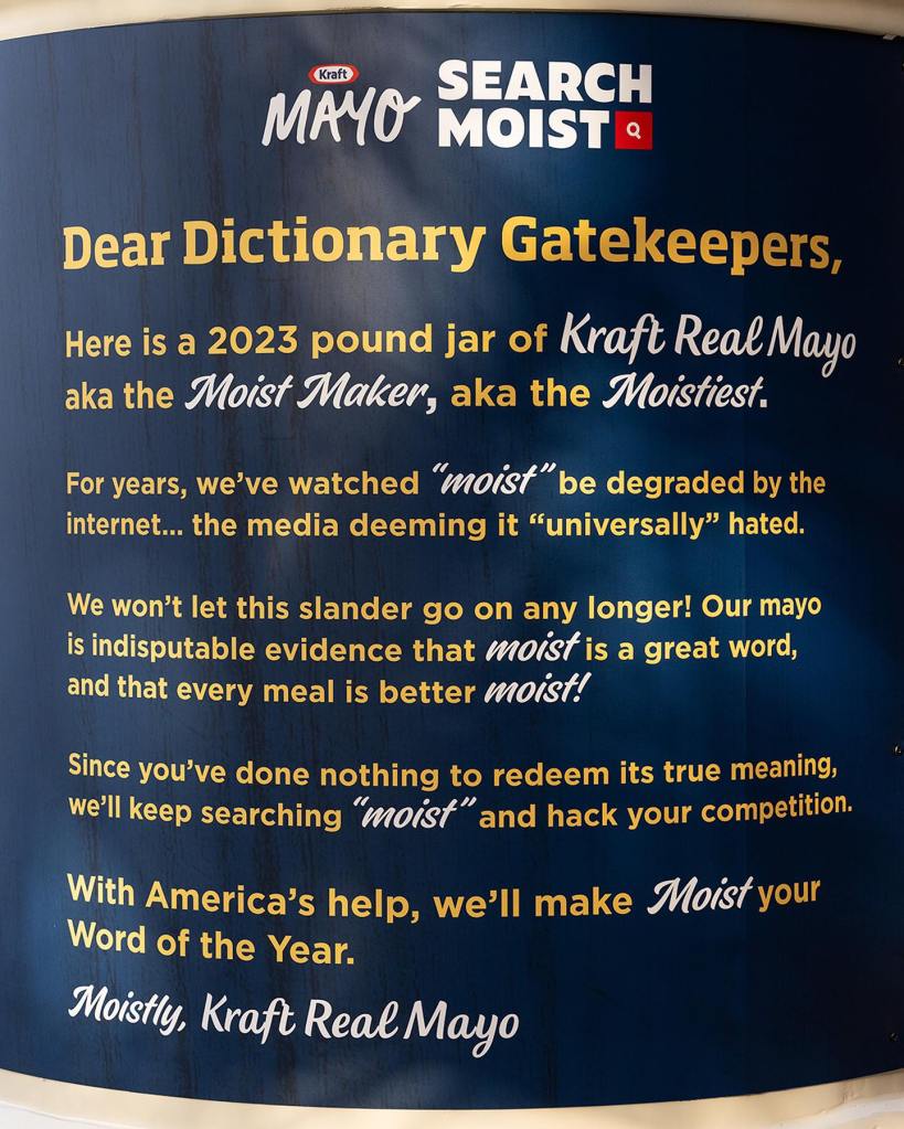 Close up of the back of the 8 ft. Kraft Mayo jar that was placed in front of Merriam-Webster's dictionary. It reads:

Here is a 2023 pound jar of Kraft Real Mayo aka the Moist Maker, aka the Moistest. 

For years, we've watched "moist" be degraded by the internet... the media deeming it "universally" hated. 

We won't let this slander go on any longer! Our mayo is indisputable evidence that moist is a great word, and that every meal is better moist!

Since you've done nothing to redeem its true meaning, we'll keep searching "moist" and hack your competition.

With America's help, we'll make Moist your Word of the Year.

Moistly, Kraft Real Mayo