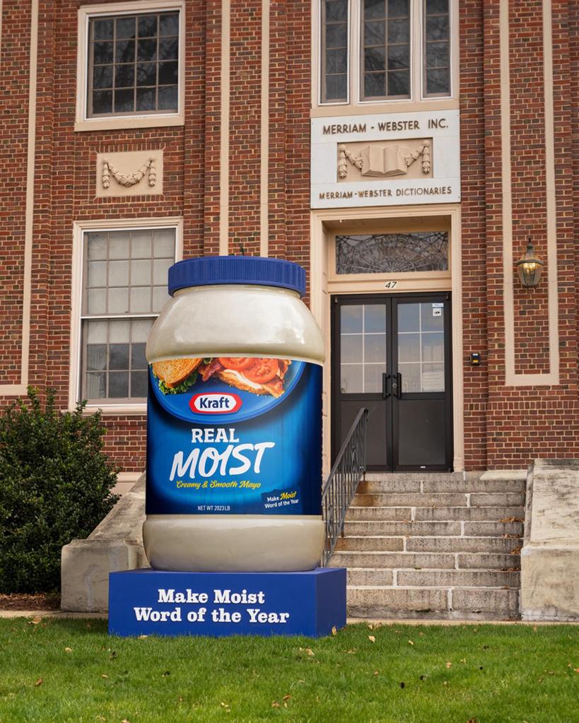 An 8 ft. jar of Kraft May sat in front of the staircase of Merriam-Webster's headquarters. The front of the jar reads "Real MOIST." The platform it's on reads "Make Moist Word of the Year"