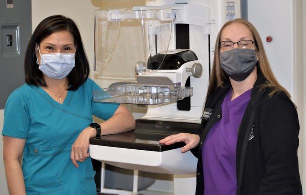 Image shows two technicians standing with a mammogram machine.