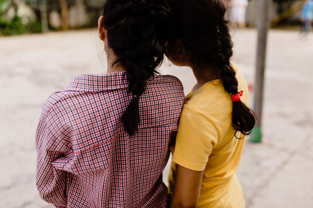 view from the back of two girls with braids leaning against each other