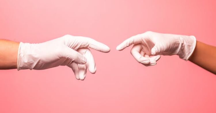 Image shows two hands, wearing rubber gloves reaching toward one another.