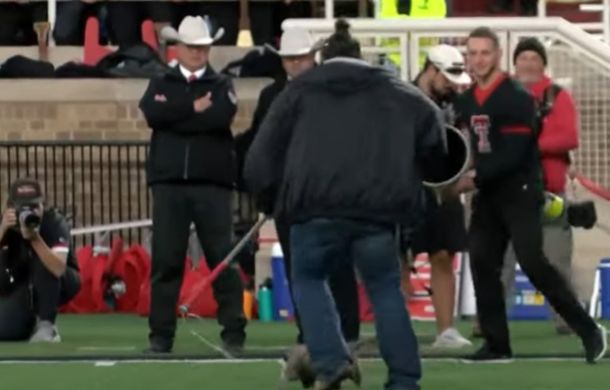 Image shows stadium personnel chasing an opossum on a football field before capturing the animal in a pole snare.