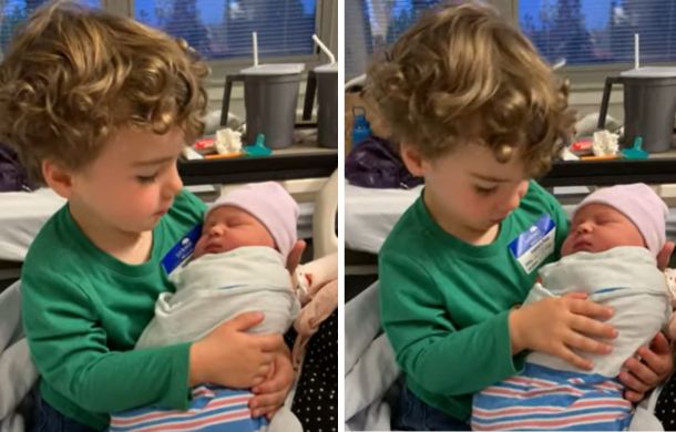 Image shows a young boy holding his newborn sister. He is searching for something his sister is missing... arms.