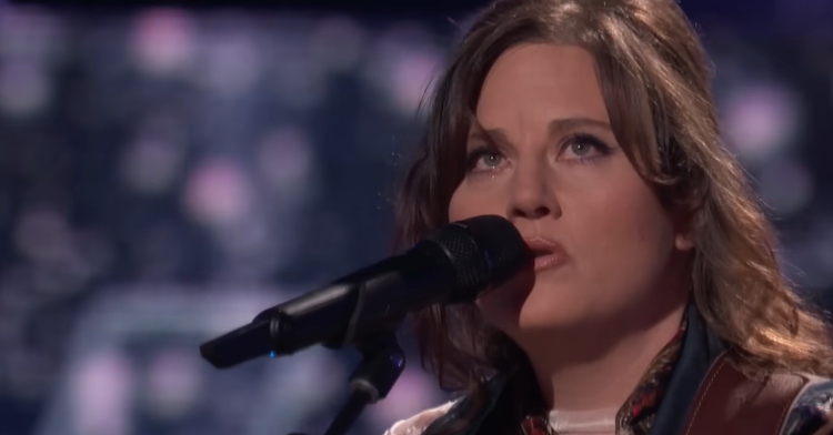 Close up of Alexa Wildish singing into a mic on "The Voice" stage. She looks emotional, and it appears there is a single tear falling from her right eye.