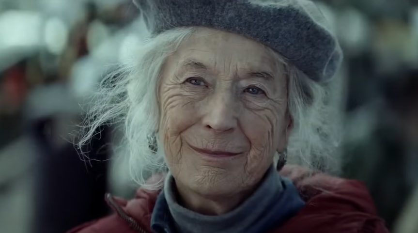 An elderly woman smiles outdoors during the holiday season in an Amazon Christmas ad.