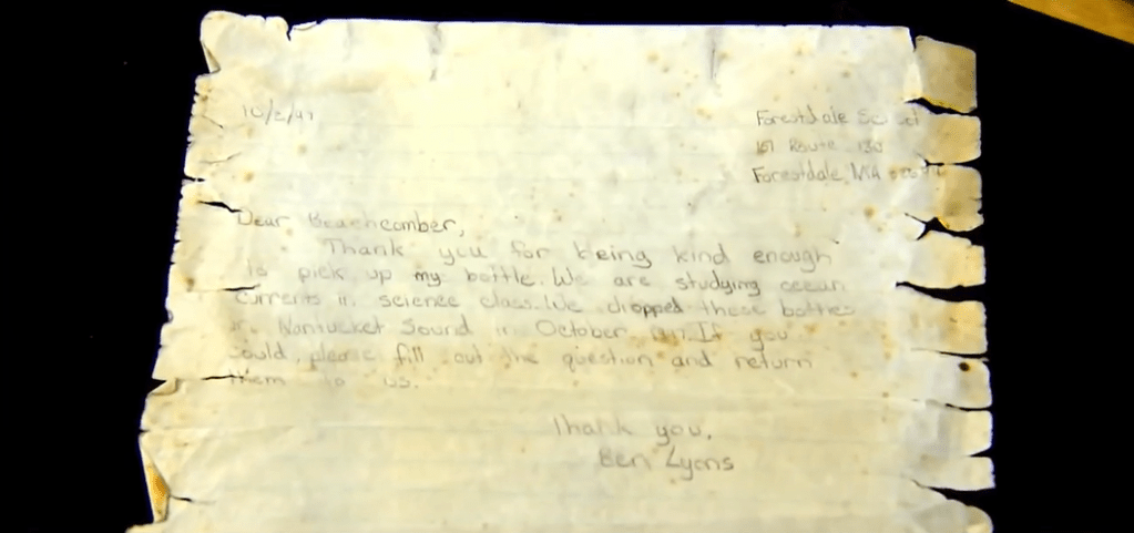 Top-down view of Ben Lyons' letter from 1997. It's torn at the edges and is yellow. It reads:

"Dear Beachgoer,

Thank you for being kind enough to pick up my bottle. We are studying ocean currents in science class. We dropped these bottles in [can't decipher] in October. If you could, please fill out the questions and return them to us. Thank you. Ben Lyons."