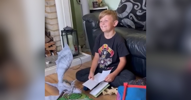 A little boy smiles as he sits on the floor, letter in hand.