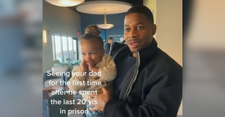 A man holds a baby in his arms, eyes wide from excitement. Text on the image reads: Seeing your dad for the first time after he spent the last 20 yrs in prison