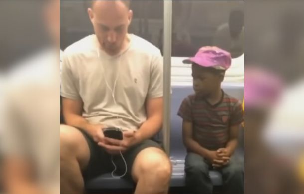 In a heartwarming moment on the subway, a young boy watches a man play a game on his phone.