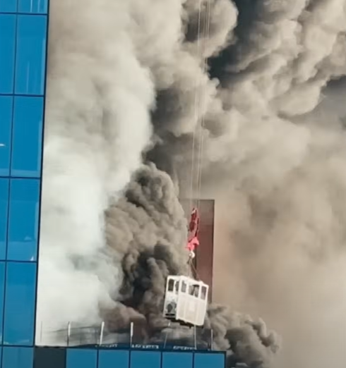 Close up view of a crane being used to lift a man form a burning building, smoke rising in the air.