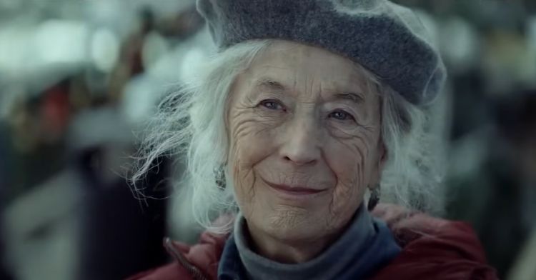 An elderly woman smiles outdoors during the holiday season.