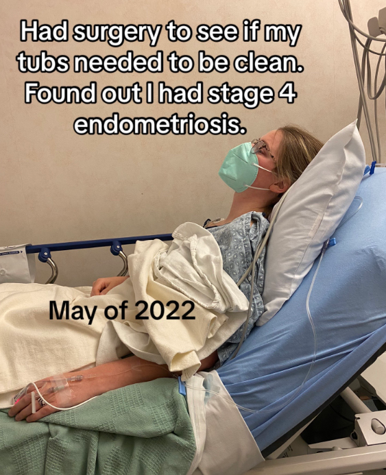 Chelsea lays in a hospital bed, hooked up to machines. She looks tired as she looks into the distance, a face mask on.
Text on the image reads: "Had surgery to see if my tubs needed to be clean. Found out I had stage 4 endometriosis. May of 2022.