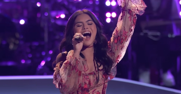 Close up of Kaylee Shimizu singing passionately into the mic on "The Voice." Her eyes are closed and she has one hand in the air.