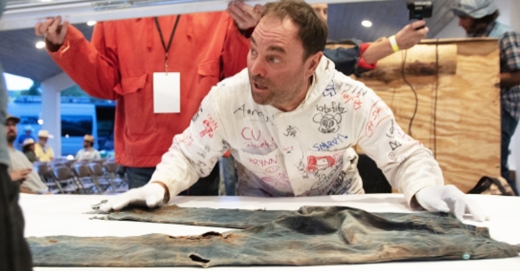 A man leans down to get closer to the oldest known pair of Levis. The jeans are laid out on a table.
