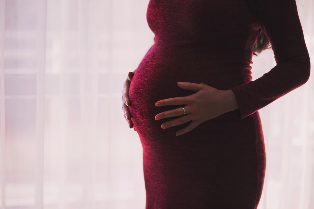 A pregnant woman wearing a red dress at work.
