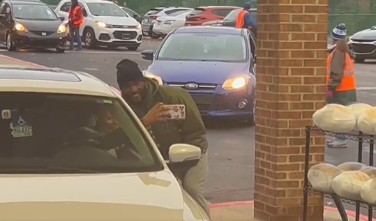 Shaq Leonard smiles as he leans down and poses for a selfie with a person in a parked car.