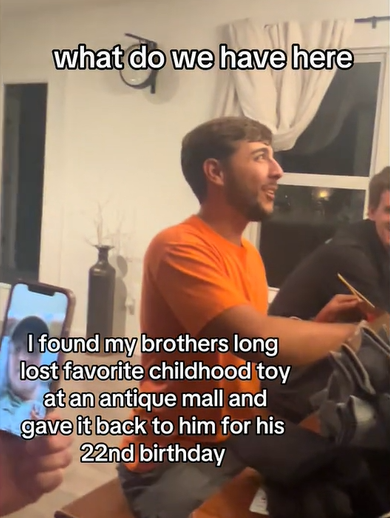 A young man looks slightly up and smiles as he reaches into a gift bag. Text on the screen shows what he's saying: What do we have here...

Other text on the screen reads:

I found my brothers long lost favorite childhood toy at an antique mall and gave it back to him for his 22nd birthday. 