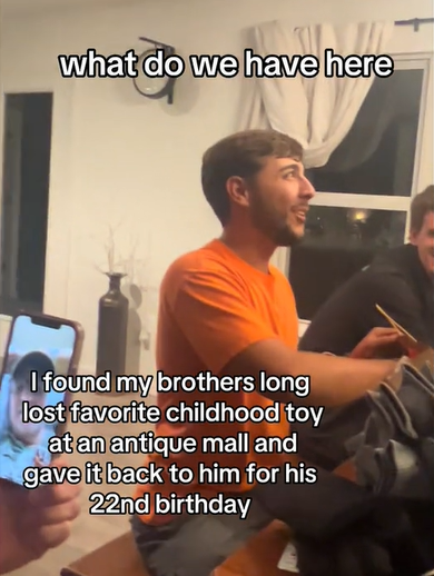 A young man looks slightly up and smiles as he reaches into a gift bag. Text on the screen shows what he's saying: What do we have here...
Other text on the screen reads:
I found my brothers long lost favorite childhood toy at an antique mall and gave it back to him for his 22nd birthday.