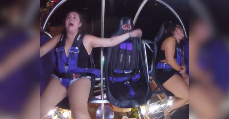 Two women mid-ride on a sling shot amusement park ride. One is laughing while the other is screaming as her arms and legs flail.