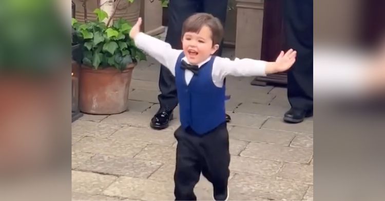 A little boy runs down the aisle at a wedding with open arms.