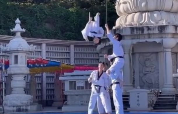 Taekwondo professionals performing an acrobatic flip combined with board-shattering kicks.